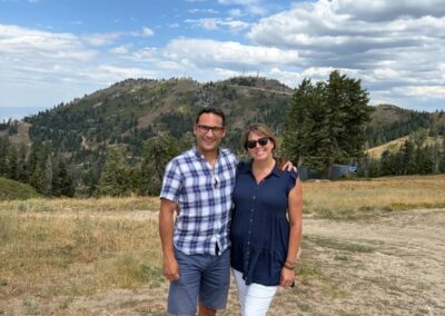 Couple standing on the mountaintop at Bogus Basin with forested hills and a big summer sky behind them